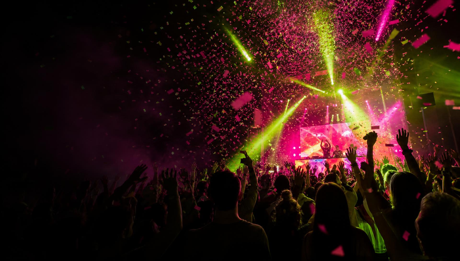 Crowd celebrating at a live event with confetti, lime and hot-pink lights, and performers on stage